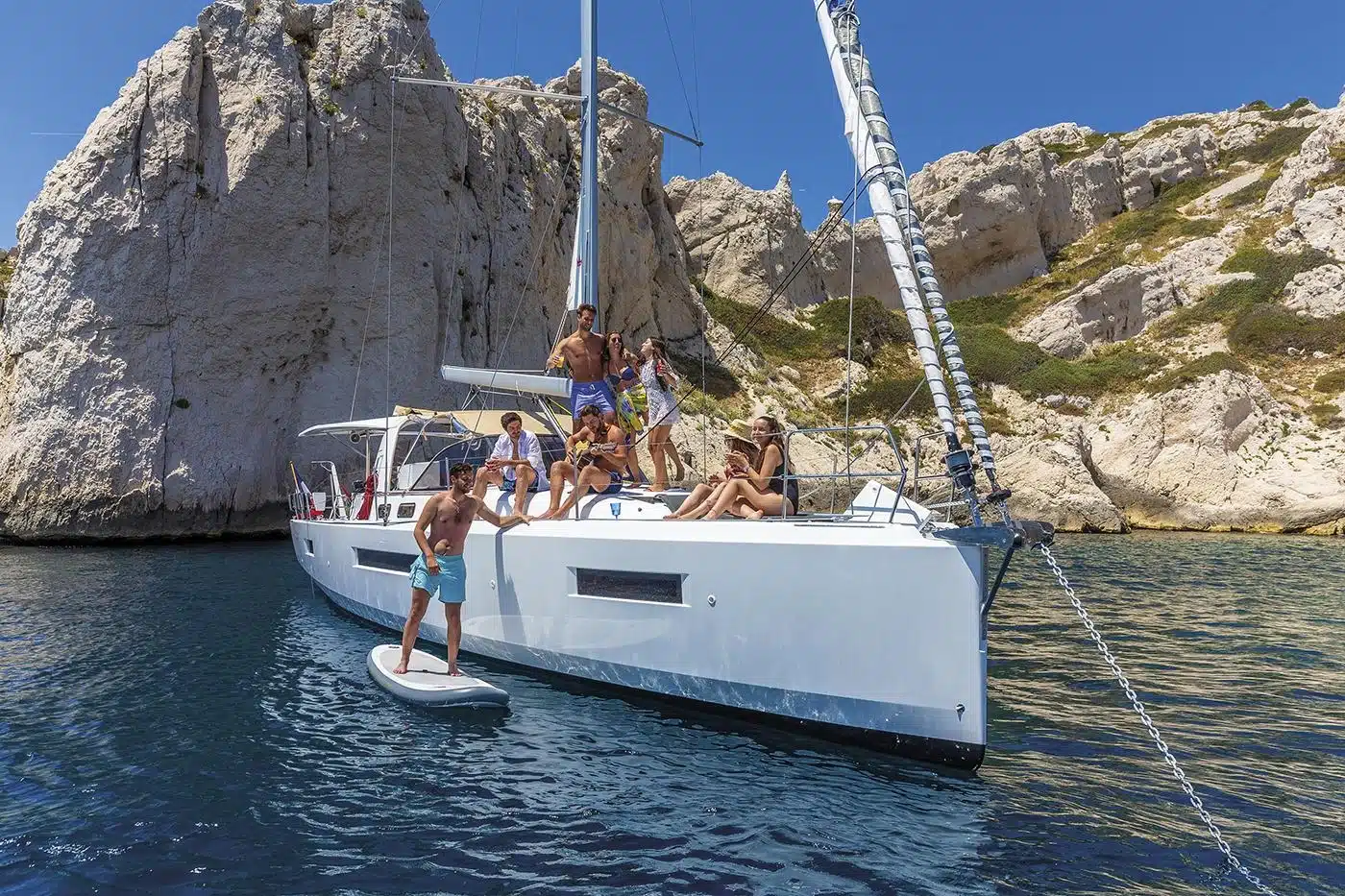 Segelschiff hat geankert und die Segelcrew macht Musik und posiert für ein Foto, ein Mitsegler steht auf einem Stand-Up-Paddle neben dem Segelboot