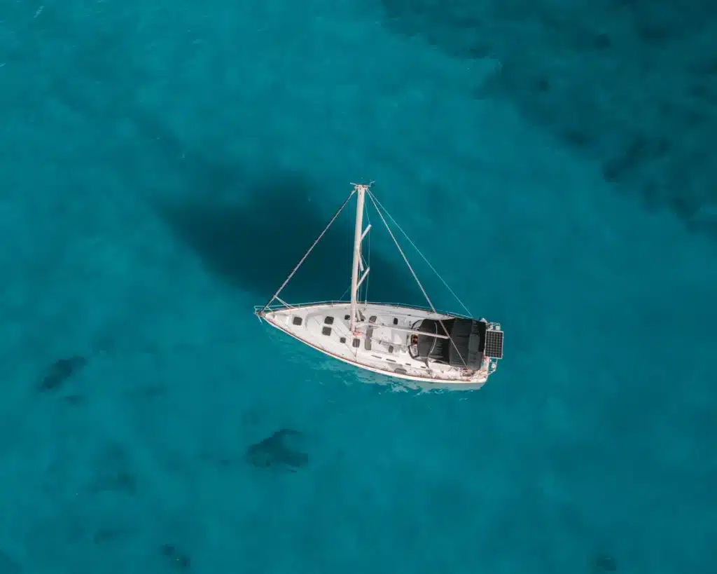 Luftaufnahme einer einsamen weißen Yacht, die auf einem leuchtend türkisfarbenen Meer segelt. Die Übersicht hebt die Isolation und die kontrastierenden Farben des Bootes und des Wassers hervor.