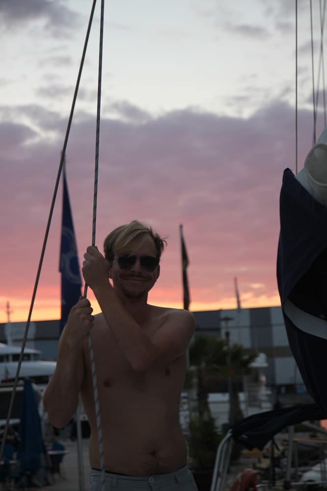 Crewmitglied hält sich an einer Leine an Bord fest und genießt die Abendstimmung mit tollem Abendrot