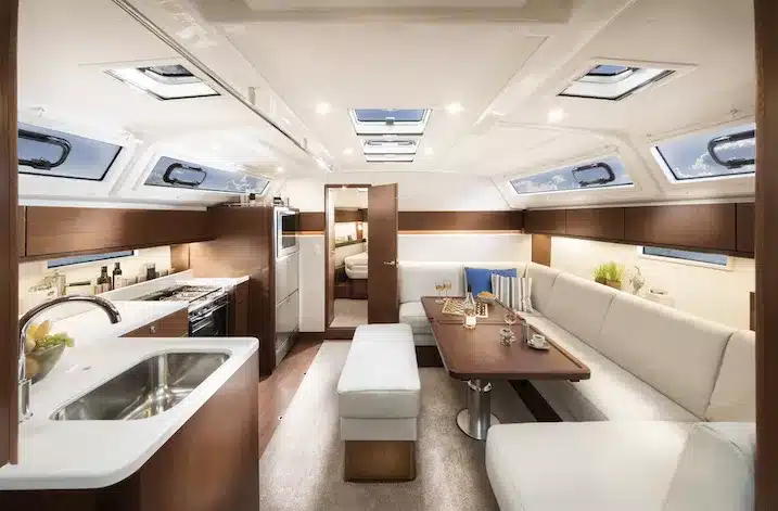 Innenansicht einer luxuriösen Yacht mit einer gut ausgestatteten Küche mit Spüle auf der linken Seite und einem Essbereich mit Sofa und Tisch auf der rechten Seite. Natürliches Licht strömt durch mehrere Fenster oben während Ihres Seg