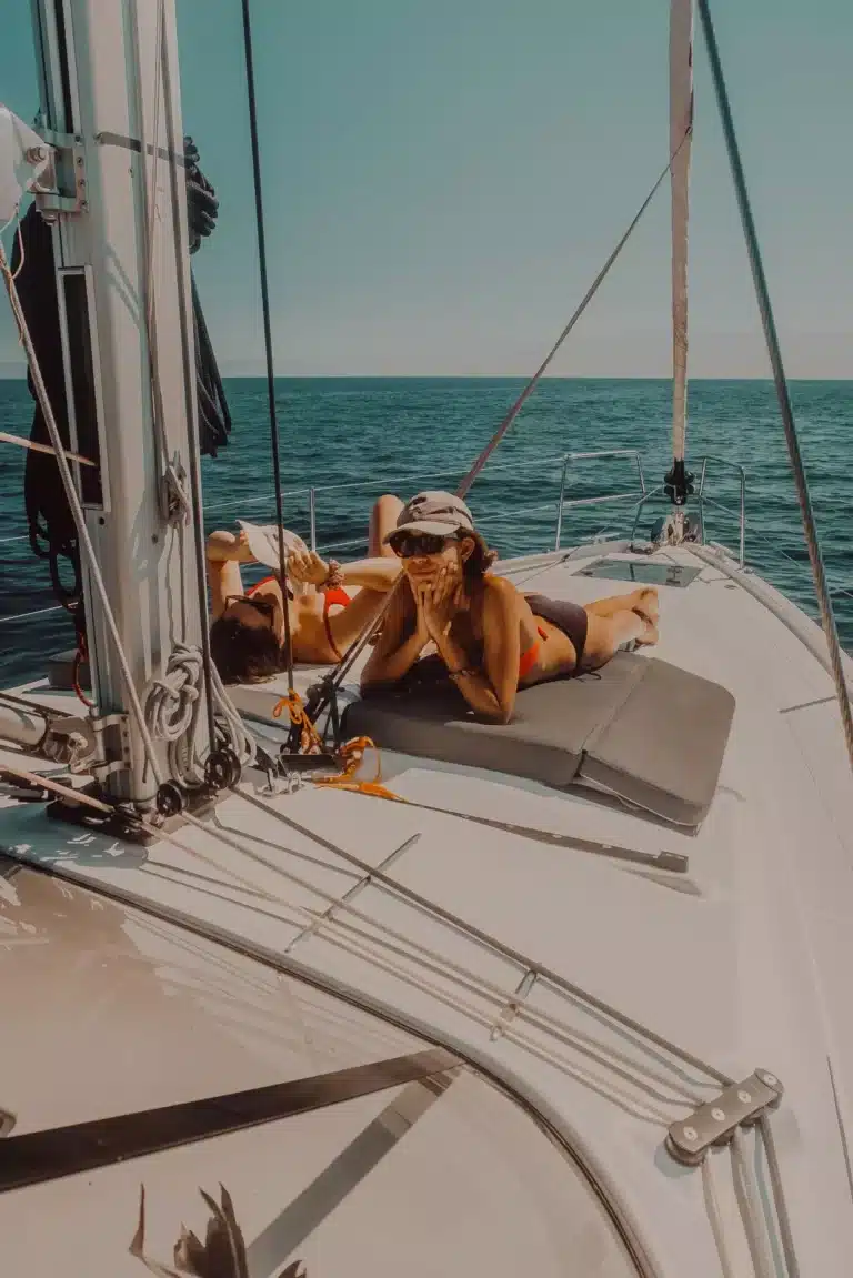 Zwei Menschen entspannen sich auf dem Deck eines Segelboots, genießen die Sonne und den Meerblick während ihres Segelurlaubs. Diese friedliche Szene fängt die Freizeit auf See ein.