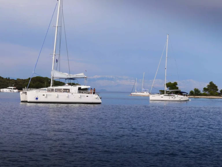 Zwei Segelboote ankerten in der Nähe einer kleinen Insel mit üppigem Grün in ruhigem blauen Wasser, unter einem klaren Himmel mit fernen Bergen im Hintergrund, bereit für eine Segelreise.