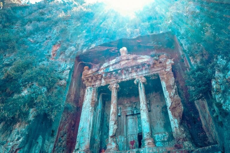 Antikes, in den Felsen gehauenes Grab mit einer verzierten Fassade mit Säulen und Giebel, hoch oben in einem lebendigen, felsigen Berg unter einem klaren blauen Himmel während eines Segeltörns.