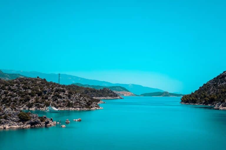 Ein ruhiger türkisfarbener See, eingebettet zwischen üppigen grünen Hügeln unter einem klaren blauen Himmel, perfekt für einen Segeltörn.