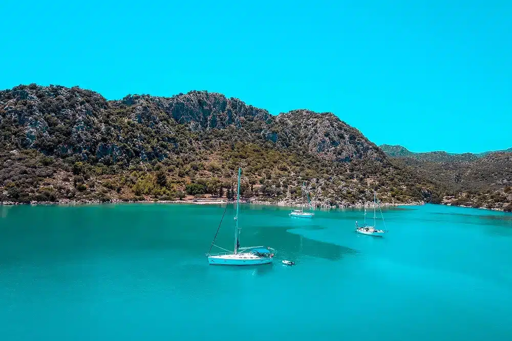 Drei Segelboote ankerten in einer ruhigen, türkisfarbenen Bucht, umgeben von schroffen Hügeln unter einem klaren blauen Himmel, und waren bereit zum Segeln.