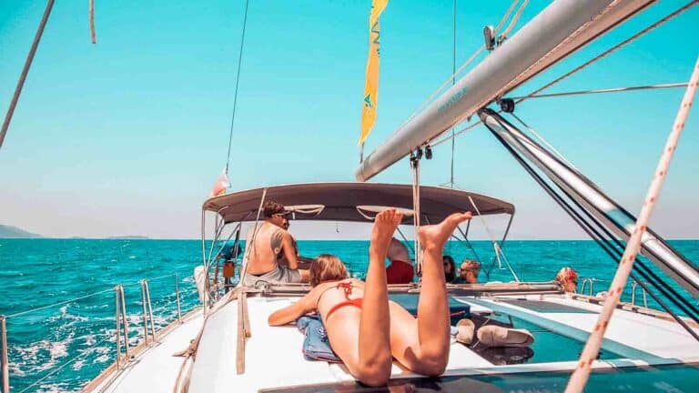 Eine Gruppe von Menschen entspannt auf dem Deck einer Segelyacht, umgeben vom klaren blauen Himmel und dem Meer, und genießt einen sonnigen Tag auf dem Wasser.