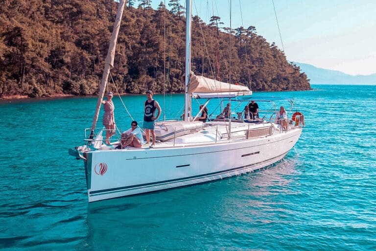 Eine Gruppe von Menschen genießt einen Tag auf einer Segelyacht, umgeben von klarem, türkisfarbenem Wasser mit üppigen grünen Hügeln im Hintergrund.