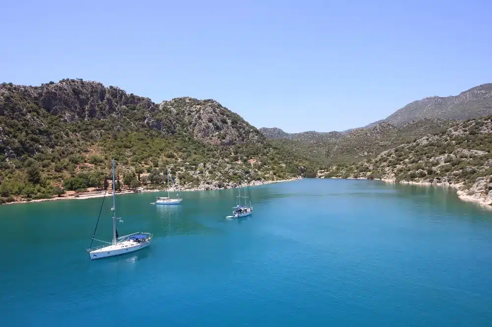 Eine ruhige Bucht mit türkisfarbenem Wasser, umgeben von üppigen grünen Hügeln, mit mehreren Segelbooten vor Anker unter einem klaren blauen Himmel, perfekt für einen Segeltörn.