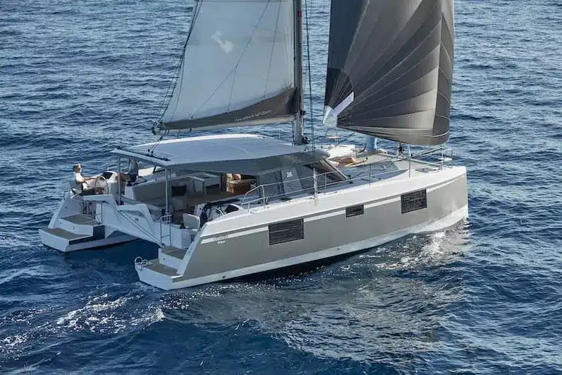 Ein moderner Katamaran mit großen Segeln gleitet durch das tiefblaue Wasser und präsentiert seine geräumigen Decks und sein elegantes Design – perfekt für einen Segelurlaub.