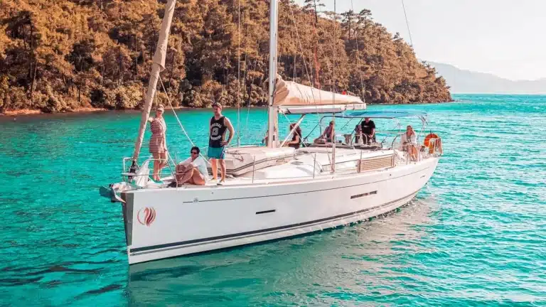 Eine Gruppe von Menschen genießt während ihres Segelurlaubs einen sonnigen Tag auf einem Segelboot im kristallklaren, türkisfarbenen Wasser.
