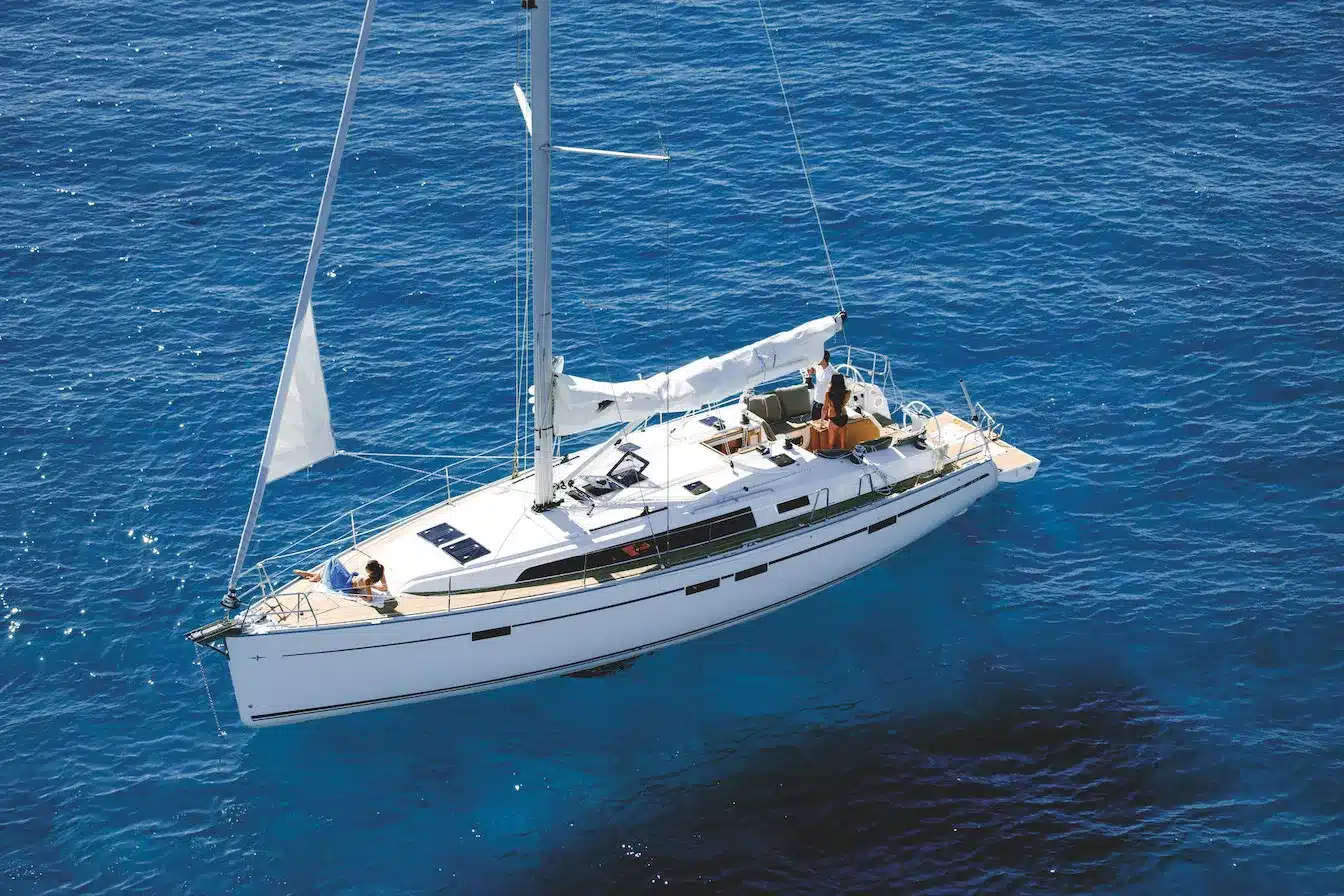Eine weiße Segelyacht mit teilweise gesetzten Segeln gleitet durch das tiefblaue Meer. Das Deck ist mit minimalen Details der Bordeinrichtung sichtbar.