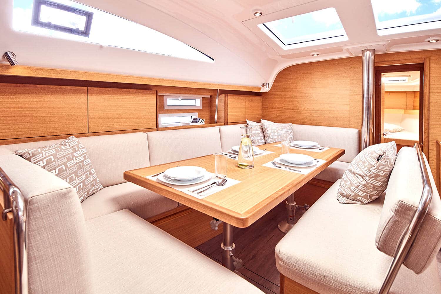 Innenansicht einer luxuriösen Segelyacht mit einem Essbereich mit einem Holztisch für vier Personen, umgeben von cremefarbenen Sofas, sanfter Beleuchtung und holzgetäfelten Wänden.
