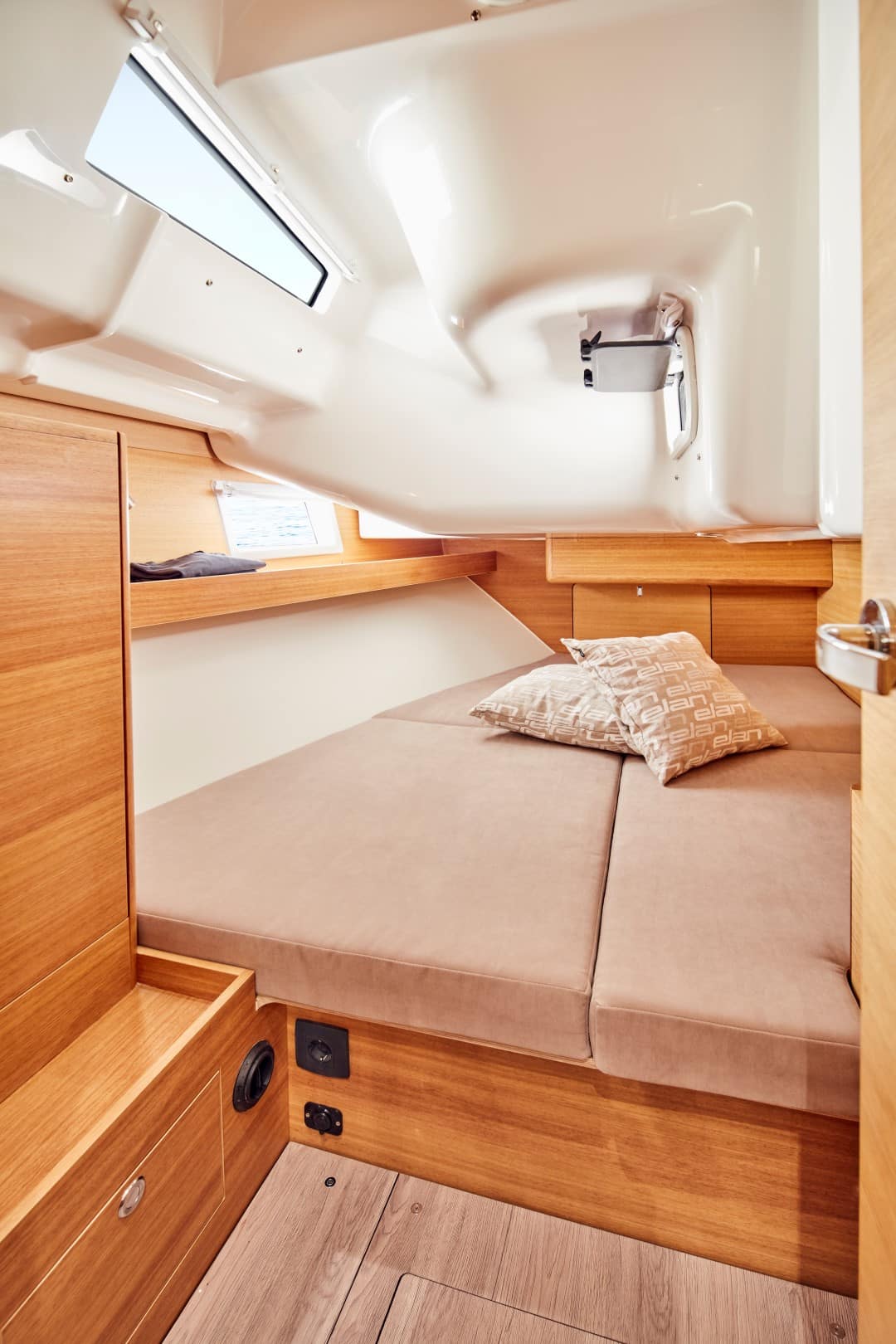 Innenansicht einer gemütlichen Segelyachtkabine mit einem ordentlich gemachten Bett mit beigem Kissen, Holzpaneelen und einem Oberlicht, das den begrenzten, aber gut gestalteten Raum hervorhebt.