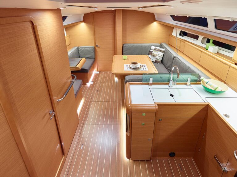 Innenansicht einer modernen Segelyacht mit gut ausgestatteter Küche mit Spüle, Essbereich mit bequemen Sitzgelegenheiten und elegantem Holzboden. Helles und geräumiges Ambiente, das durch natürliches Licht noch verstärkt wird.