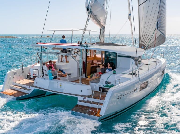 Ein moderner Segelyacht-Katamaran mit Leuten, die an Bord entspannen und unter klarem Himmel auf dem blauen Ozean kreuzen.