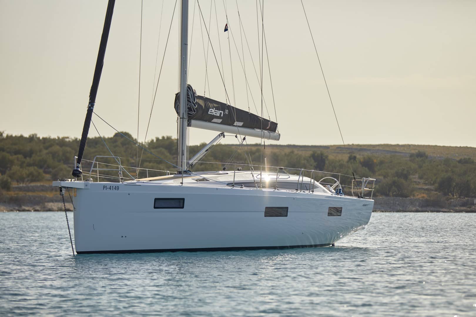 Ein modernes Segelboot mit heruntergelassenen Segeln, an einem sonnigen Tag in Küstennähe in ruhigen blauen Gewässern vor Anker liegend, perfekt für einen Segeltörn.