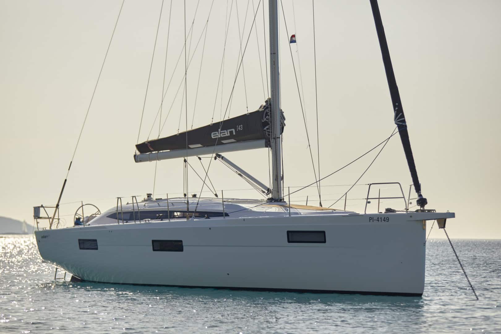 Eine weiße Segelyacht vor Anker im Meer mit ruhigem Wasser und einem unscharfen Hintergrund während der goldenen Stunde. Das Segelboot hat ein elegantes Design und die untergehende Sonne am Horizont schafft eine ruhige Kulisse.