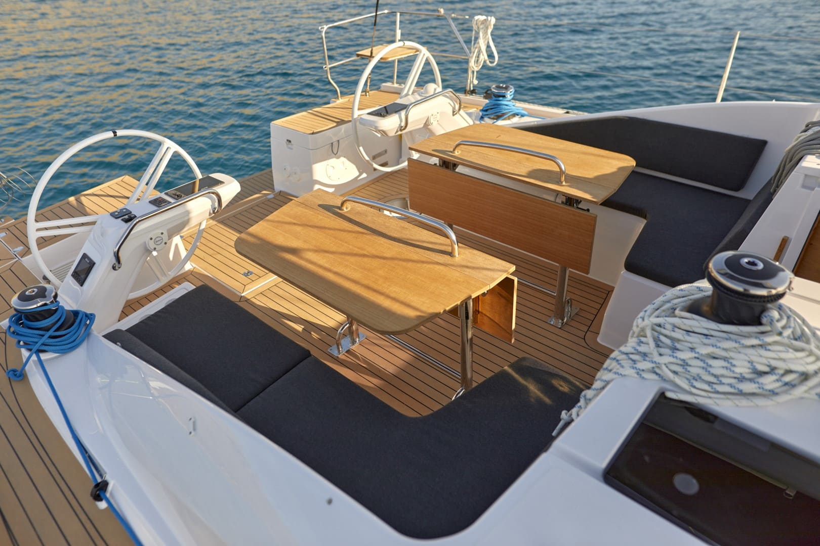 Das Heck eines Luxus-Katamarans verfügt über zwei Steuerräder, elegante Holzdecks und bequeme Sitzbereiche, mit dem ruhigen Meer im Hintergrund bei Sonnenuntergang.