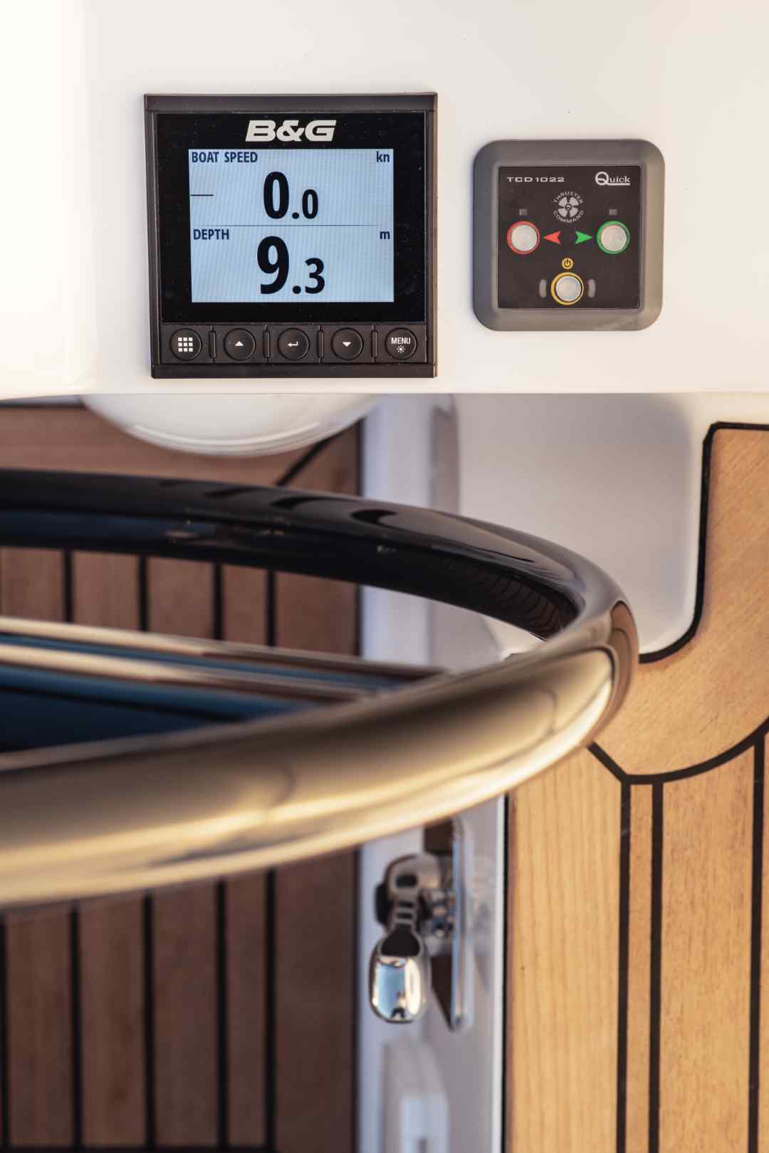 Das Bedienfeld eines Bootes auf einer Segelyacht zeigt ein B&G-Display, das eine Bootsgeschwindigkeit von 0,0 Knoten und eine Tiefe von 9,3 Metern anzeigt, neben einer Steuerung mit roten und grünen Tasten, in der Nähe eines Steuerrads.