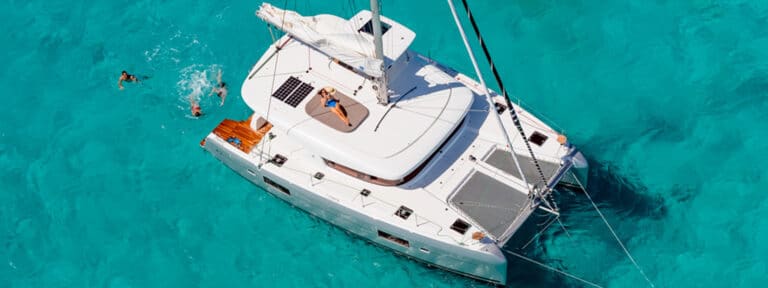 Luftaufnahme einer weißen Segelyacht im klaren, türkisfarbenen Wasser mit Menschen, die um sie herum schwimmen und schnorcheln.