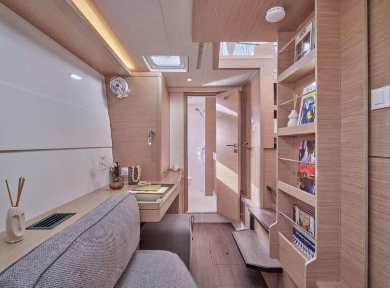 Ein modernes, kompaktes Home-Office mit einem eleganten Holzschreibtisch mit Laptop, einem bequemen grauen Sofa, eingebauten Regalen mit Büchern über Segelreise und stimmungsvoller Beleuchtung. Neutrale Töne und klare Linien schaffen einen ruhigen Arbeitsplatz.