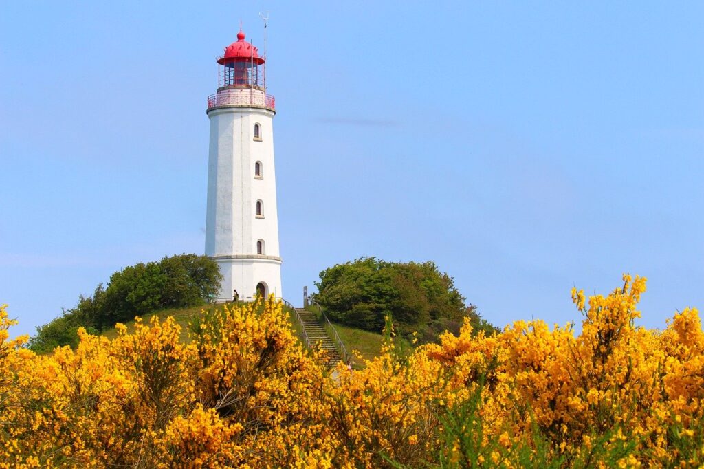Ein Leuchtturm auf einem Berg mit einer Treppe hoch. Blauer Himmel und umgeben von grünen und gelben Bäumen.