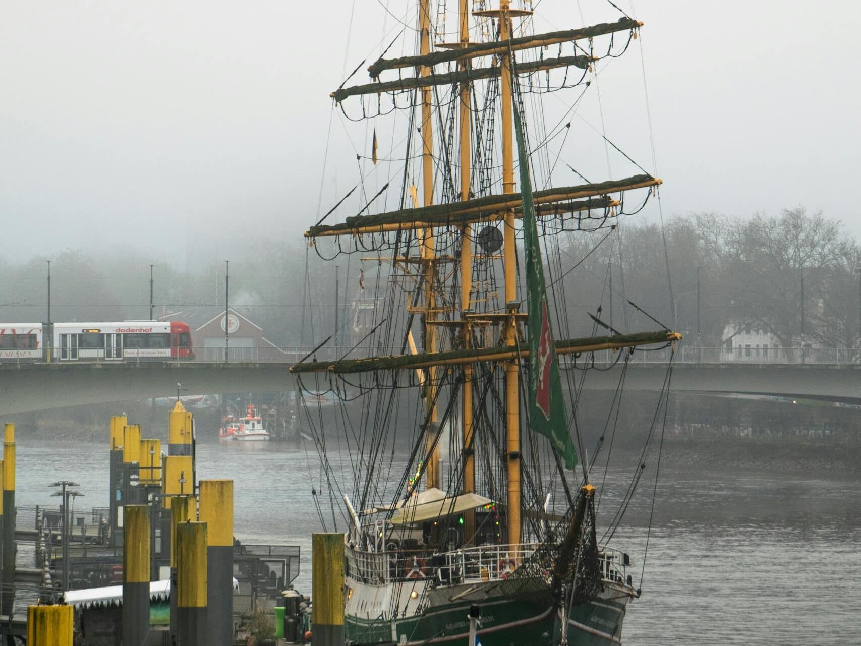 A historic tall ship docked on a misty day in Bremen, Germany, near the Weser River.