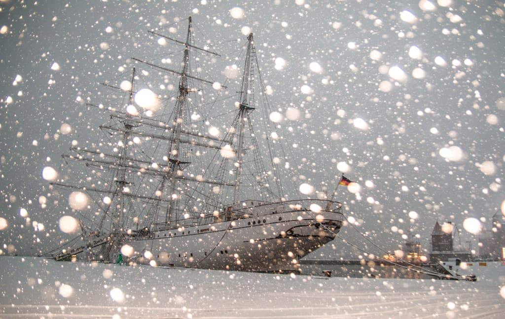 Sailing ship docked in snowy Stralsund harbor, Germany, during winter snowfall. Ostsee Wintersegeln