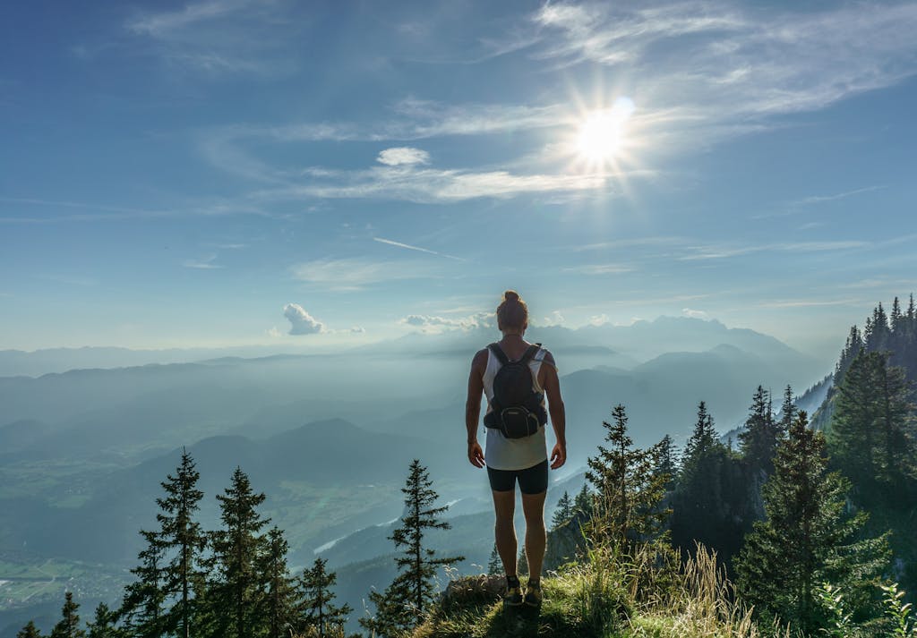 A lone hiker stands on a mountain top, overlooking a breathtaking landscape in Slovenia under the bright sun. Aktivurlaub für Sportbegeisterte: Die Top-Destinationen