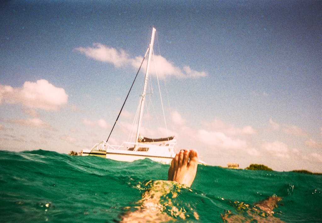 A person floating in turquoise water near a sailboat under a sunny sky.