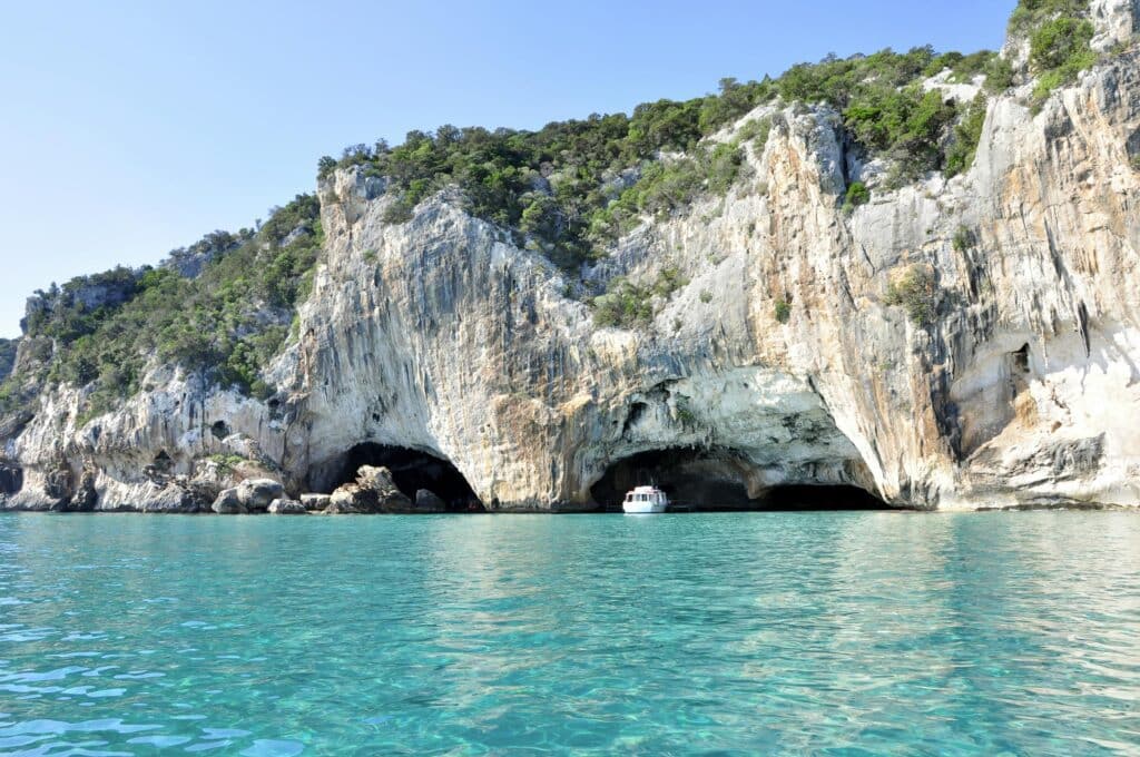 A boat enters a stunning cave along the rocky coastline of the Mediterranean Sea.