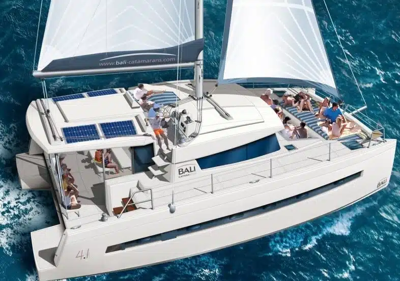 Luftaufnahme eines modernen Katamarans mit mehreren Personen, die unter offenen Segeln auf dem blauen Meer entspannen und Kontakte knüpfen.