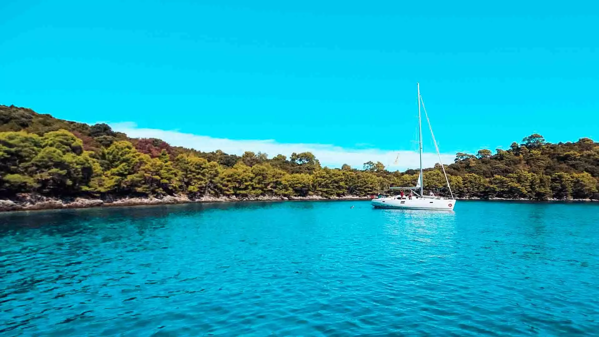 A white sailing yacht anchored in a calm turquoise bay along the green Croatian coast