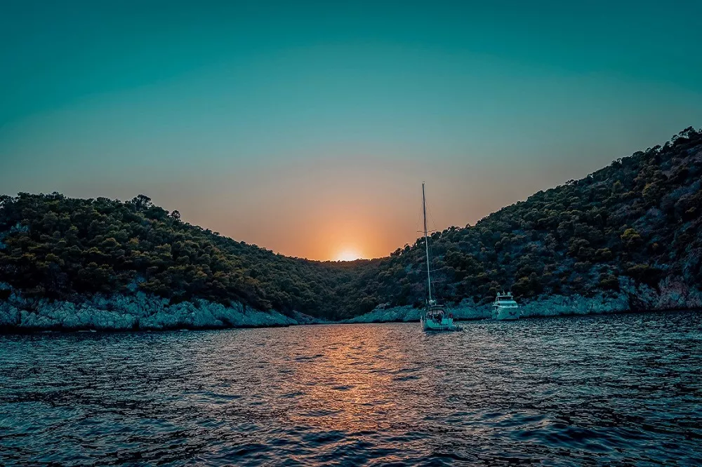 A yacht anchored at sunset in a calm Mediterranean bay